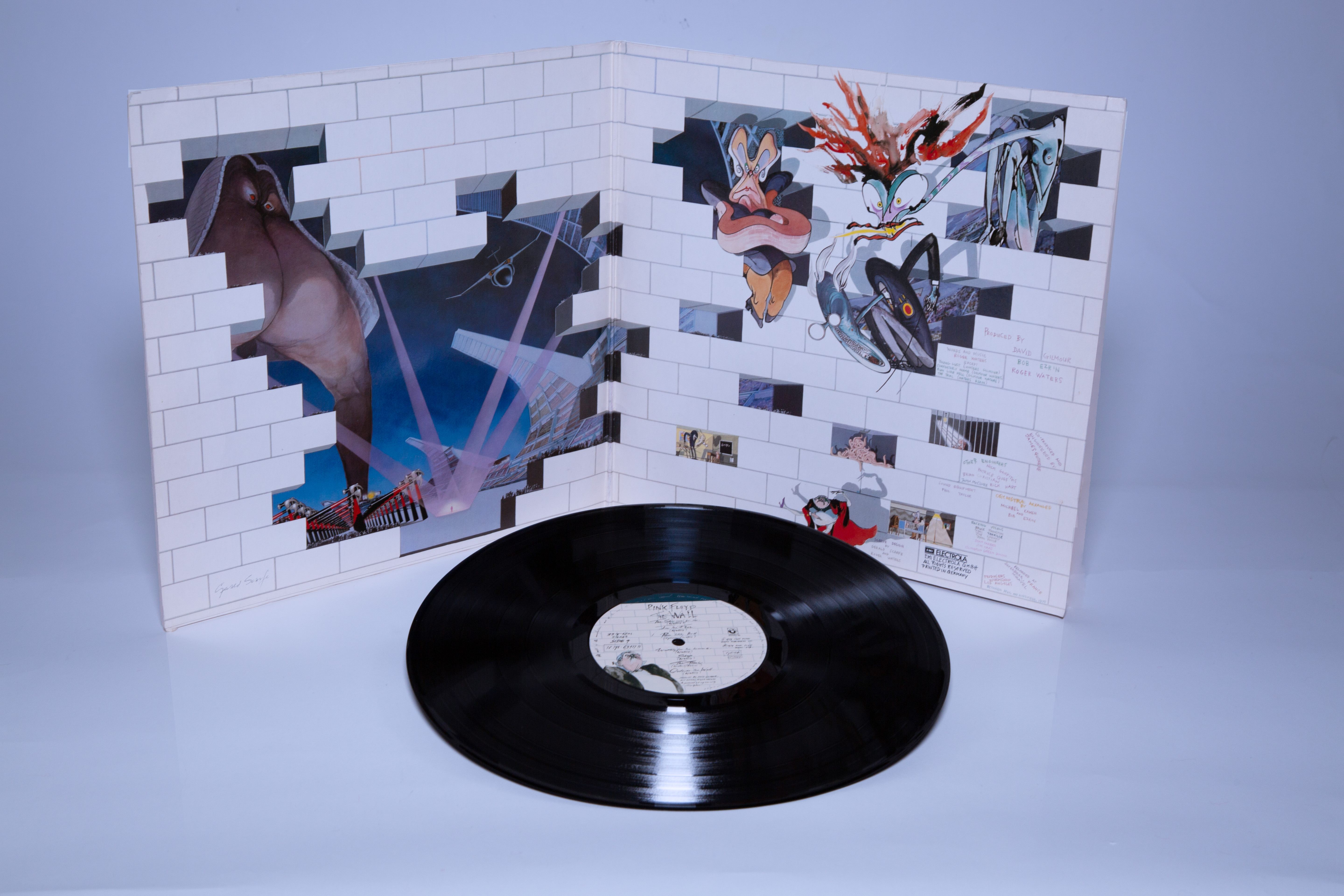 On a white background, the sleeve of Pink Floyd's The Wall is open showcasing the drawings of Gerald Scarfe. The vinyl is set in front of it.